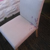 A white dining room chair with a red wine stain on the back and base